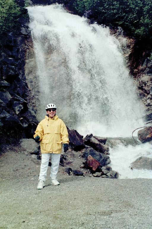 Me, standing in front of a waterfall, during the Klondike Bicycle Ride Excursion.  I am wearing a raincoat, a helmet and gloves supplied by the tour company.